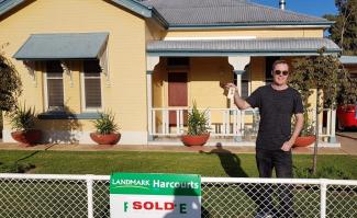 Man in front of yellow house holding keys and standing next to a SOLD sign