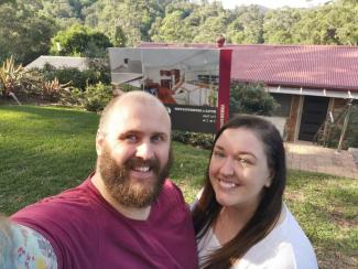 Man and woman standing in front of a 'SOLD' sign for their first home together