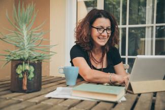 woman on laptop beside a mug, books and pot plant